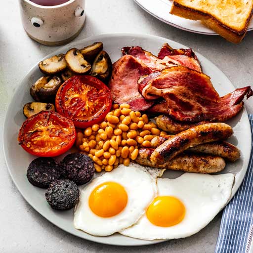 A breakfast place of eggs, sausage, ham, beans, tomatoes, and mushrooms.
