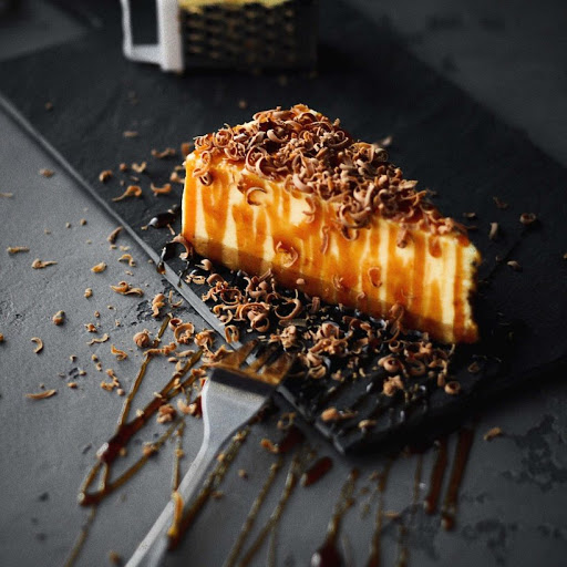A cheesecake drizzled in caramel and topped with chocolate shavings.