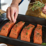 Four salmon filets being seasoned before cooking.